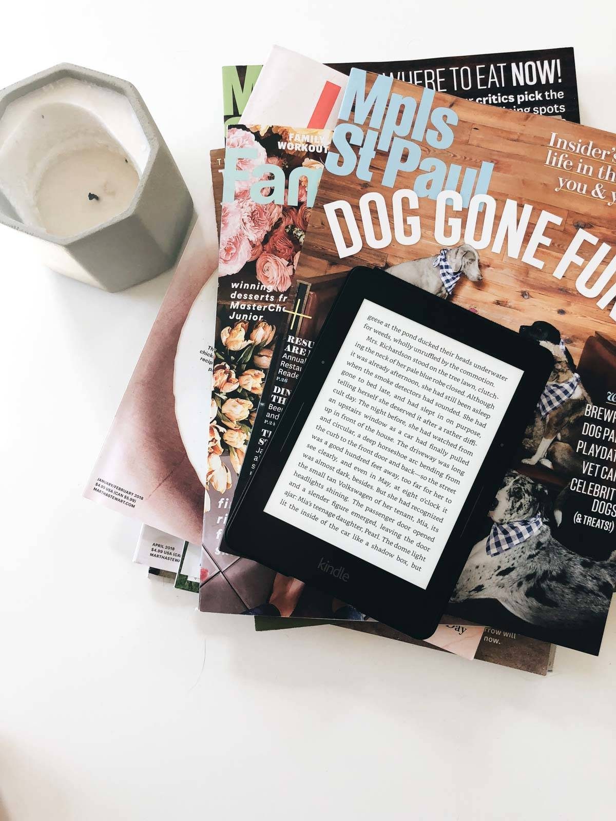 Stack of magazines with a tablet and candle.