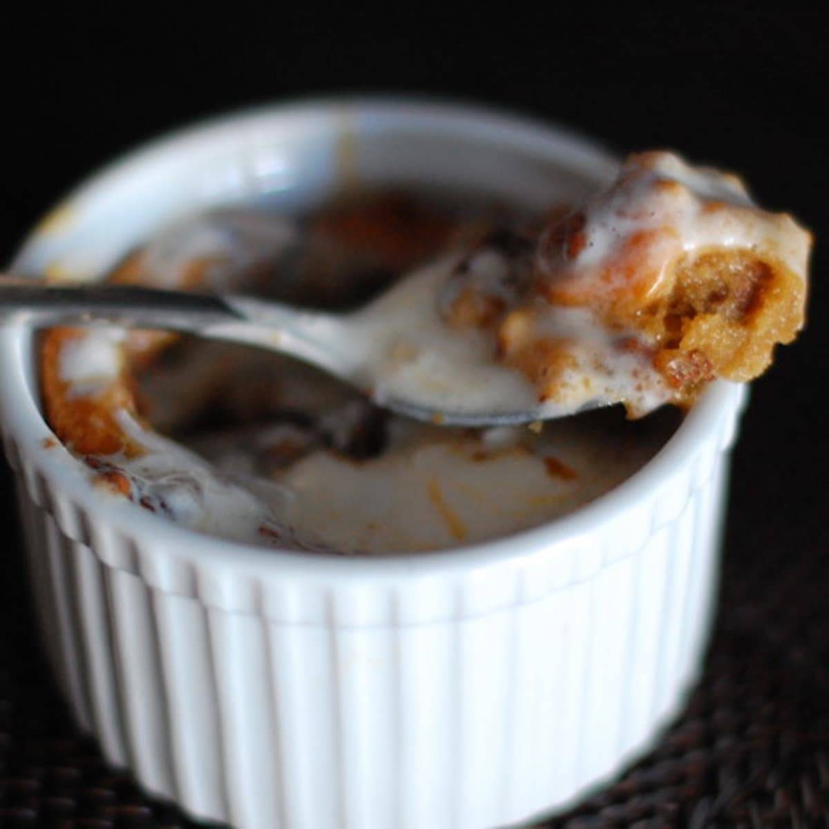 Deep Dish Chocolate Chip Cookie in a white dish with a spoon full of ice cream and caramel on top of the cookie.