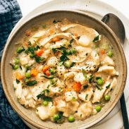 A bowl of chicken and dumplings with veggies in it.