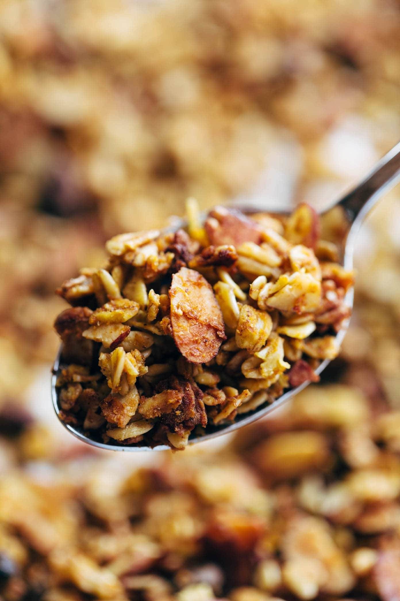 A spoon, filled with a cereal, held above a bowl of the cereal.