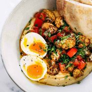 Hummus, roasted cauliflower, eggs and bread in a bowl.
