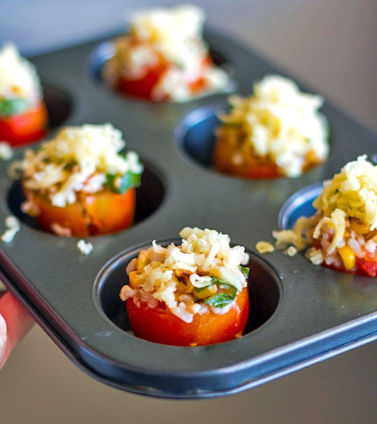 Stuffed tomatoes filled to the brim with roasted corn, fresh basil, and topped with melted Mozzarella cheese in a tin.