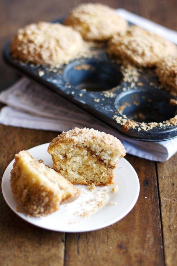 Coffee cake muffin on a white plate near a muffin tin.