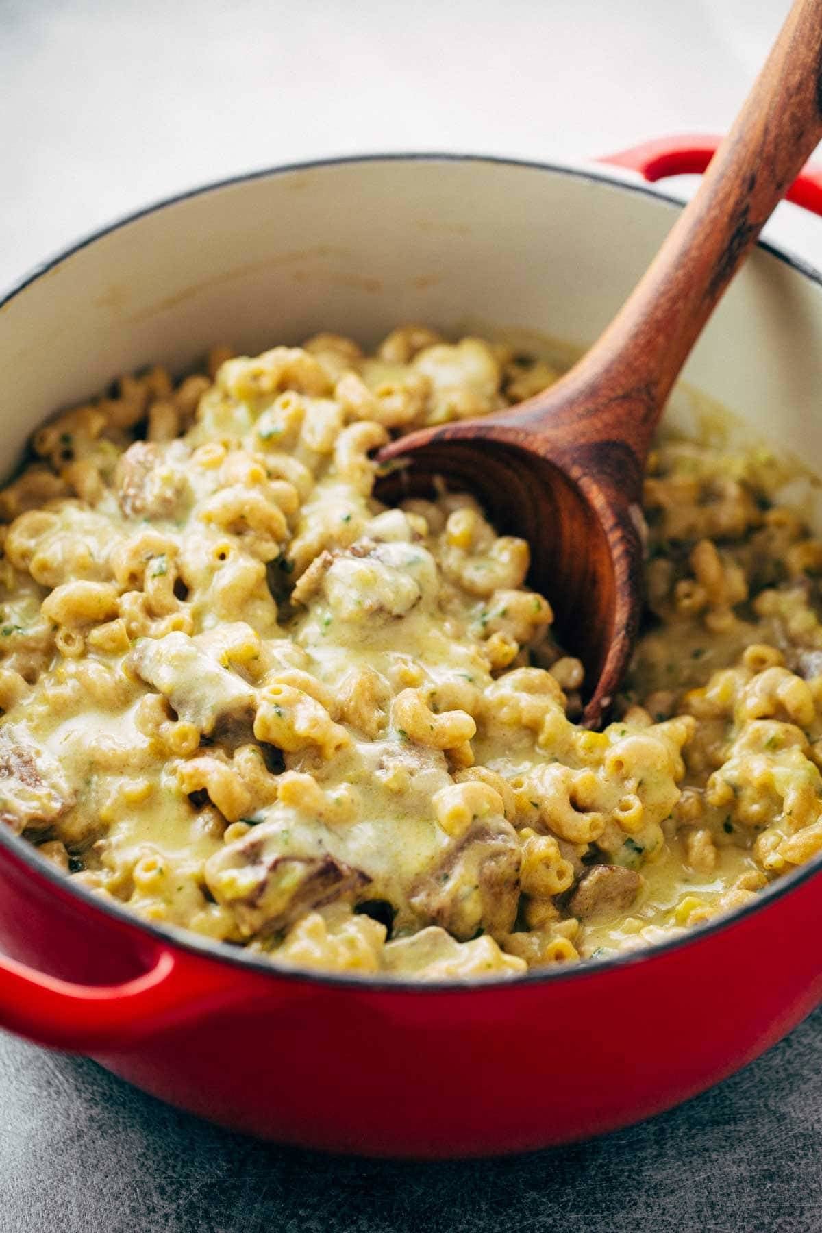 Steak and Cheddar Mac and Cheese in a red dutch oven with a spoon.