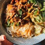 Peanut chicken in a bowl with noodles and herbs.